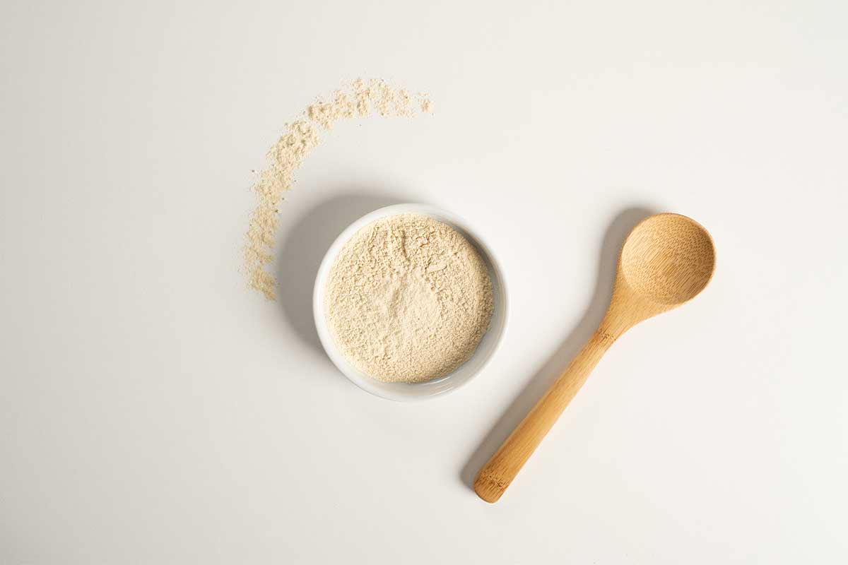 Garlic Powder in a white bowl with a wooden spoon to the lower right hand side.