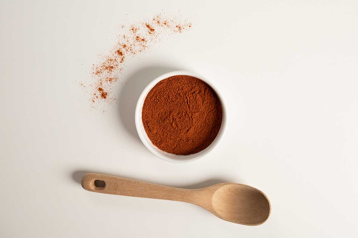 Paprika in a white bowl with a wooden spoon below it.