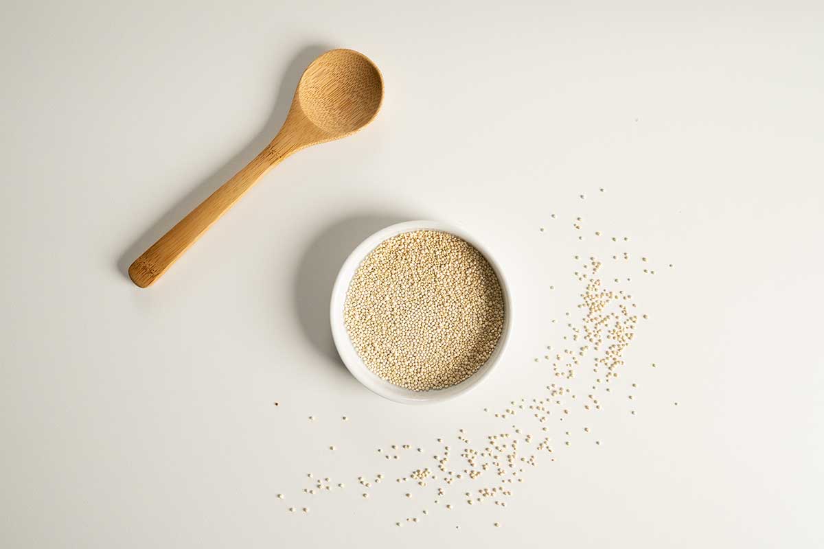 Quinoa in a small bowl with a wooden spoon on the top left.