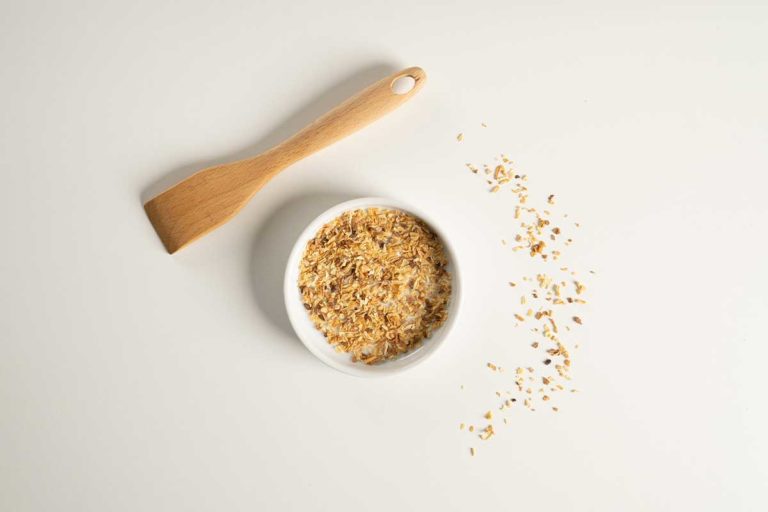 Toasted onion granules in a white bowl with a wooden spatula over the right hand side.