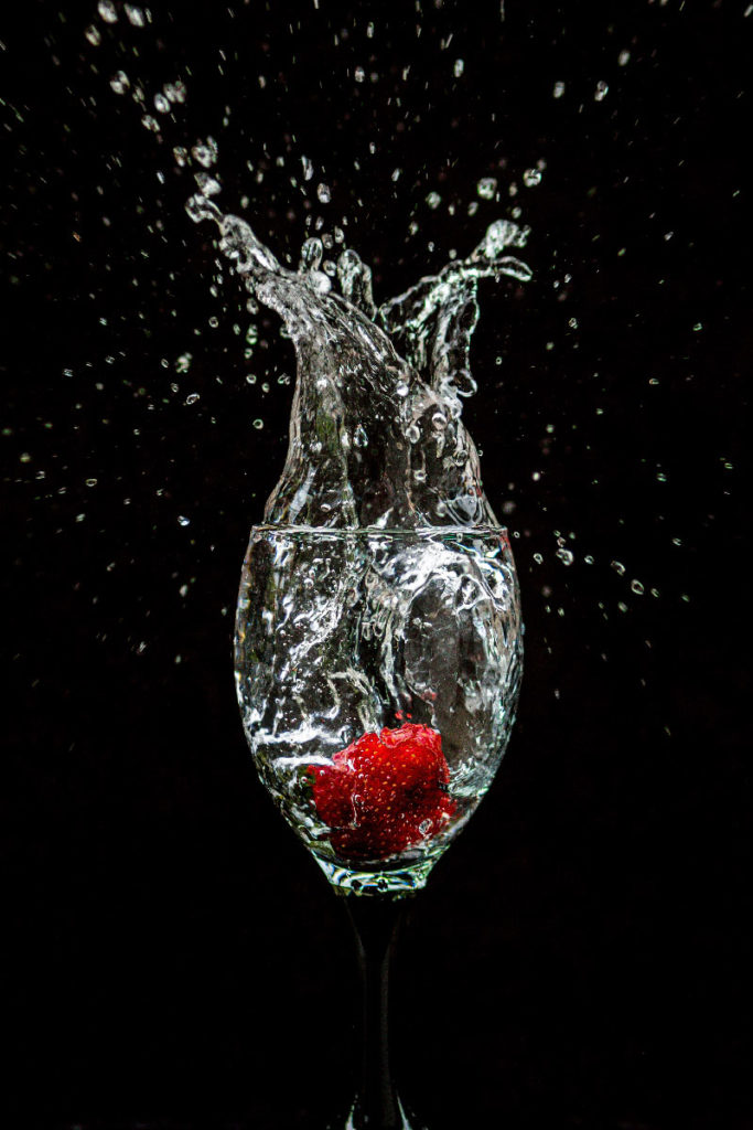 A strawberry falls into a wine glass, making a splash.