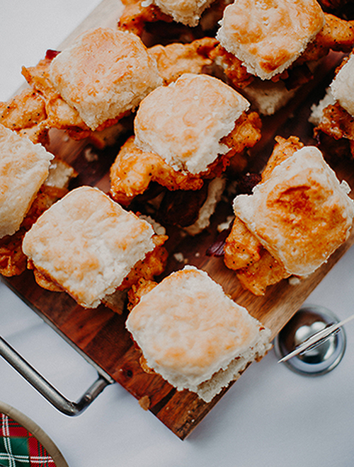 Sliders of chicken on a wooden tray.