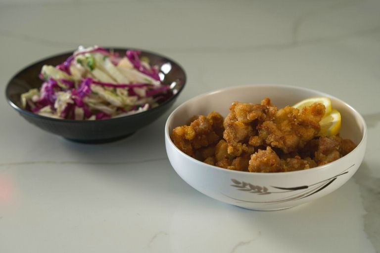 Bowl filled with Japanese Popcorn Chicken next to a bowl of Asian Slaw