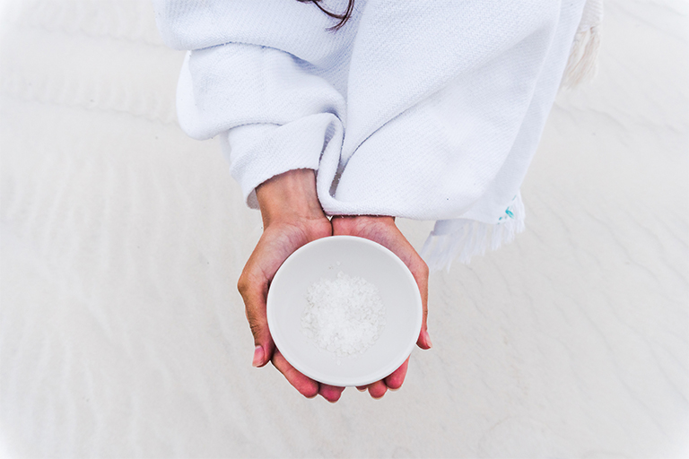 A person holds a white bowl containing salt.