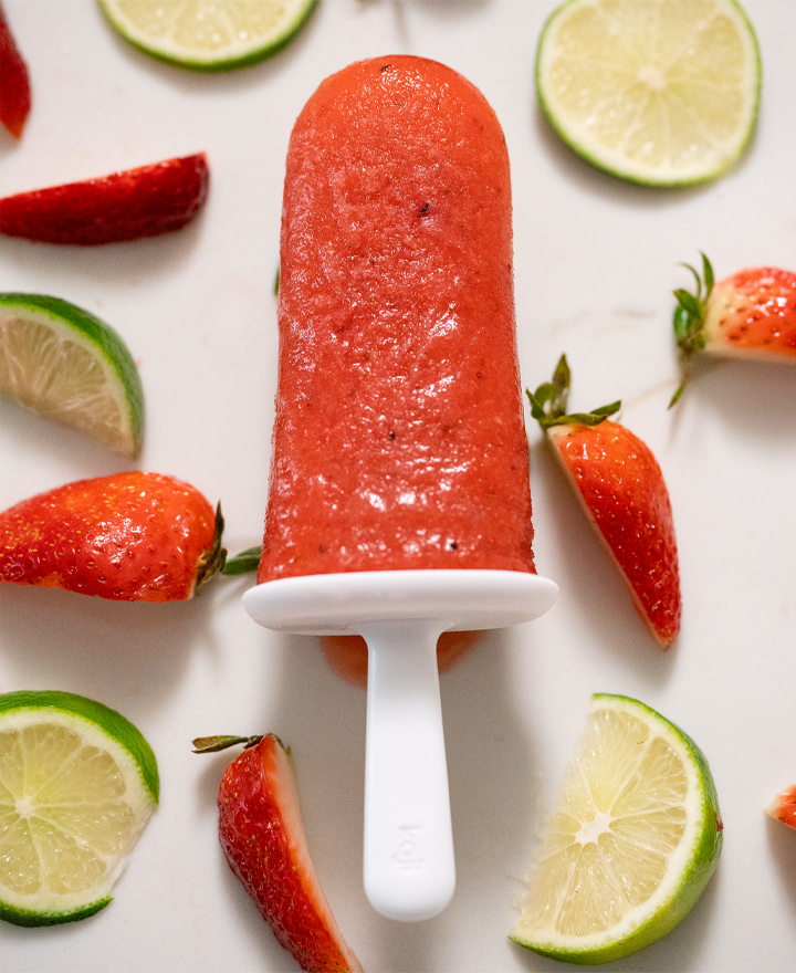 Strawberry popsicle with black pepper over slices of strawberry's and limes.
