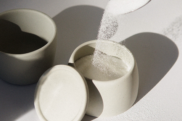 Sugar is being poured into a small white bowl/container.