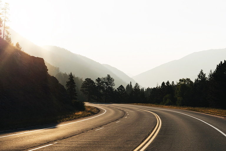 A long curved road with a view of the sunset and the landscape.