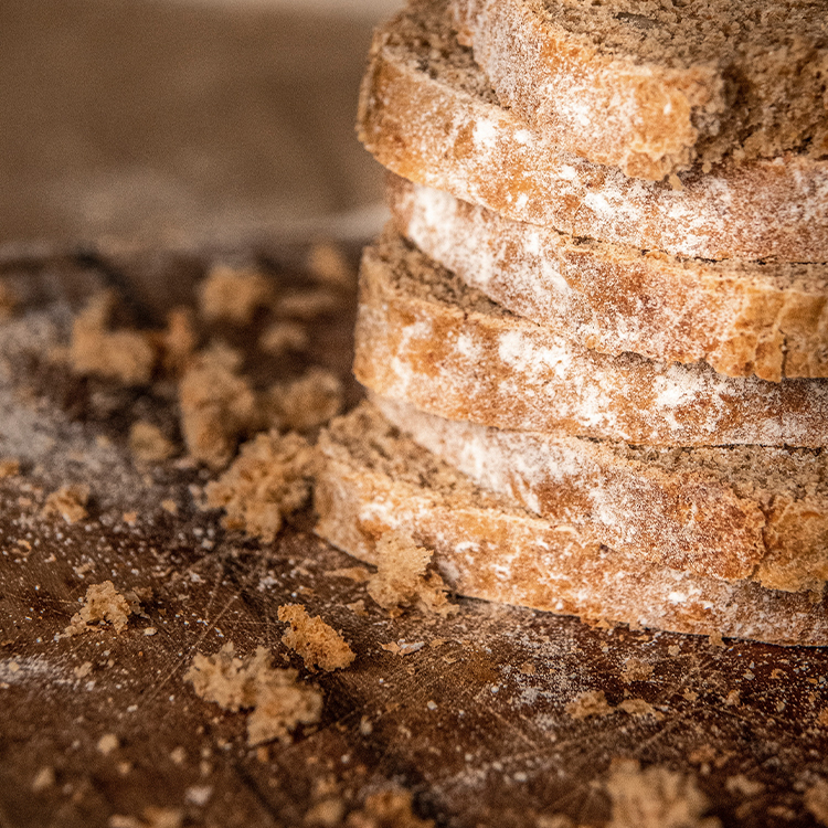 Sourdough Bread slices with white flour edges stacked on top of a brown wooden surface covered in crumbs