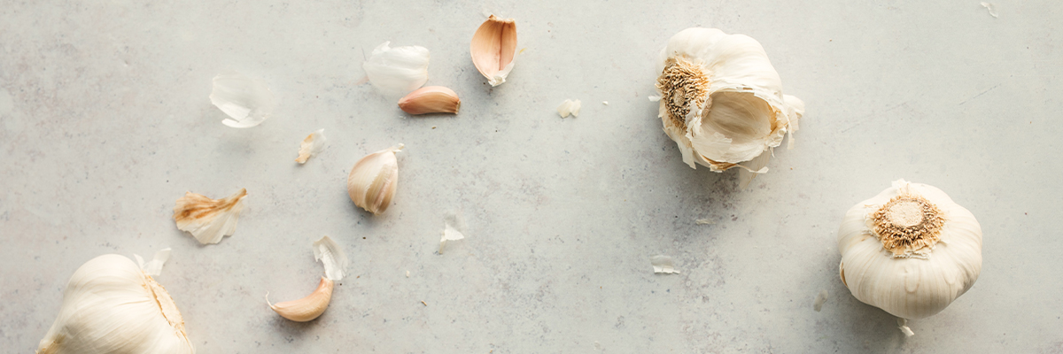 Three heads of garlic sitting on a grey counter. One has a few individual pieces broken out.