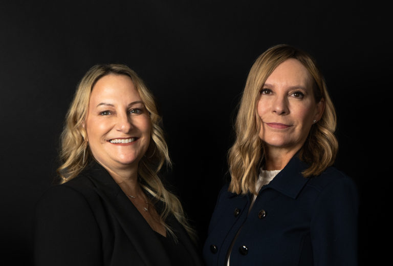 Carol Lynn and Jennifer Manns wearing black against black background, for enterprising women of the year.