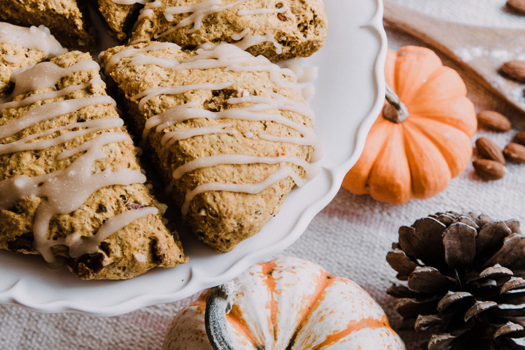 scones with tan drizzle and mini pumpkins, pinecone and almonds sitting on a textured cloth