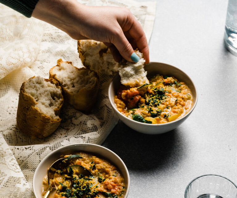 Woman's hand dipping bread in to Smoky Ratatouille Soup in a white bowl