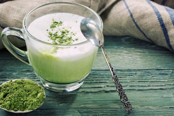 Matcha tea latte with a spoon on its rim, as green matcha powder resides next to it