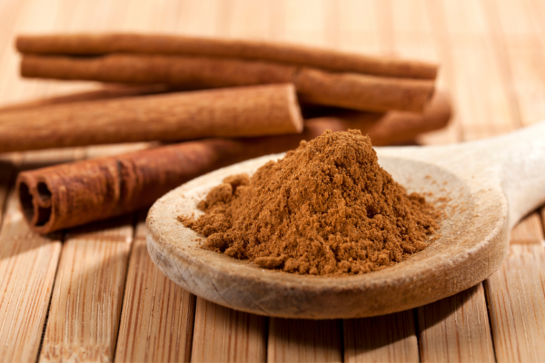 Cinnamon bunched on top of a spoon, with sticks laying beside it on a wooden table.