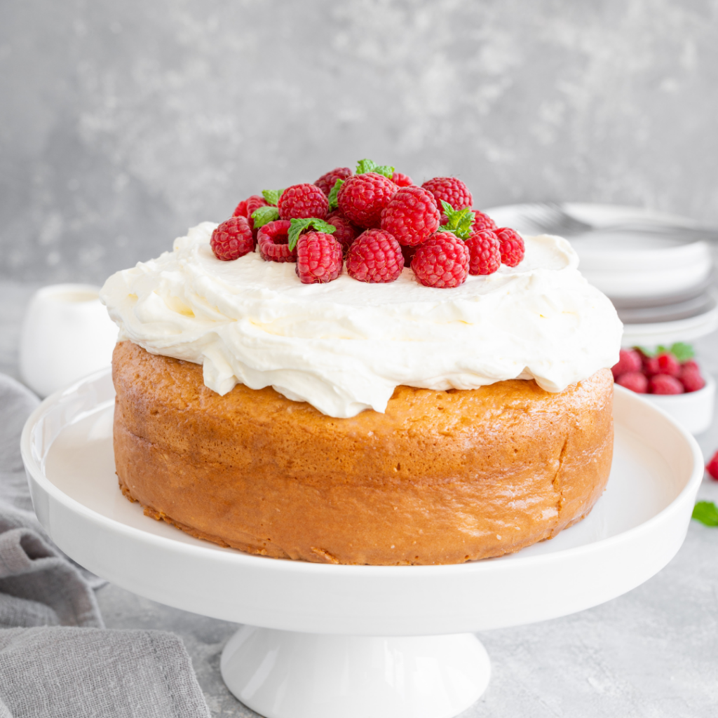 A fluffy tres leches cake with strawberries laid on top, hoisted on top of a small display.
