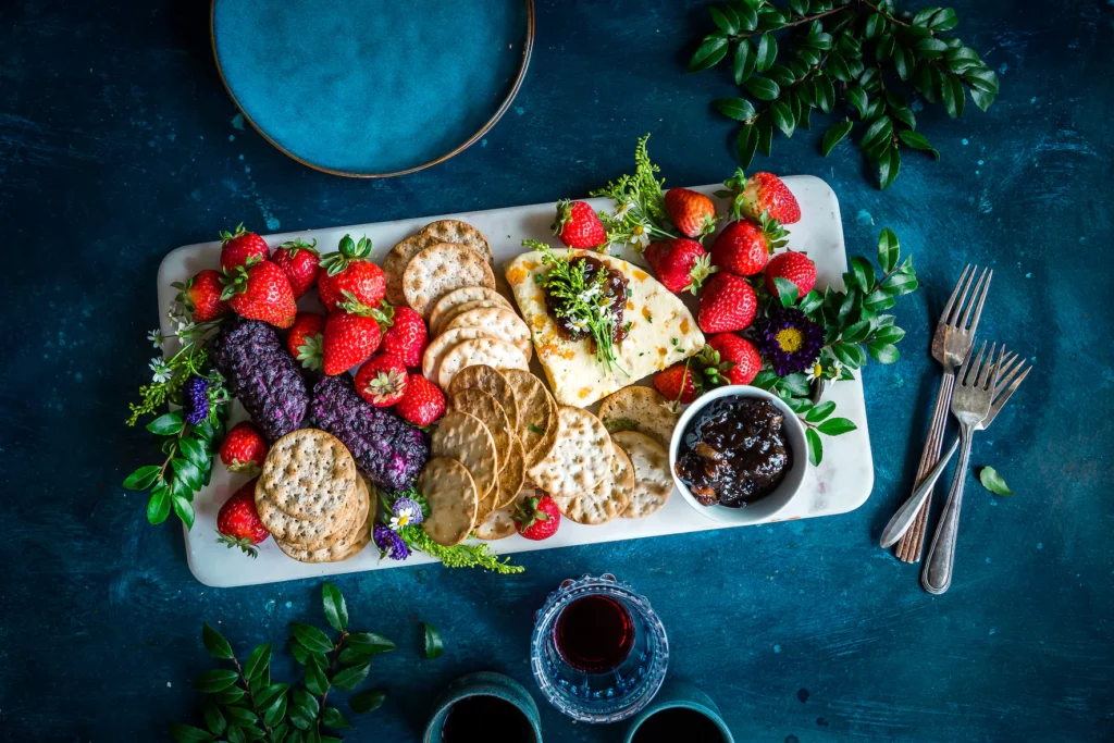 A charcuterie board tray of crackers, fruit, jams, and cheeses.