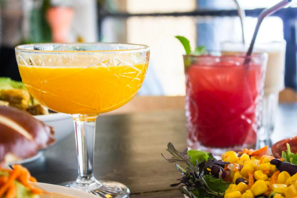 a yellow-orange cocktail on a table accompanied by a red mocktail on its right