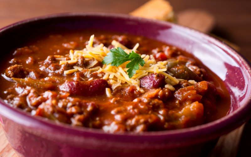 A chili dish with beans and meat contained in a red bowl.