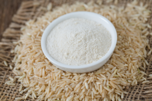 A small dish of brown rice flour sitting on top of brown rice laid underneath