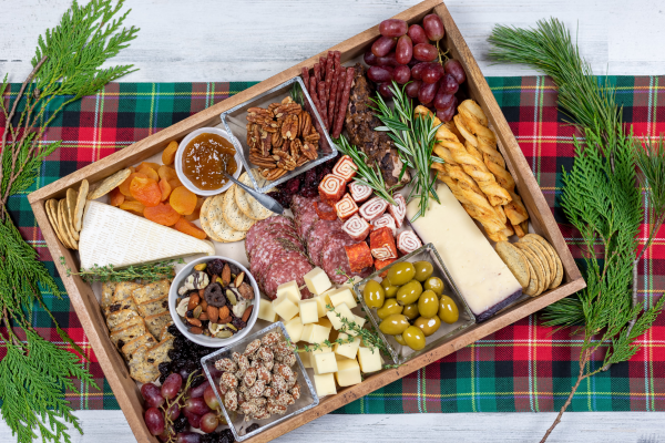 Charcuterie board on a wooden plate resting on top of a red and green plaid mantle.