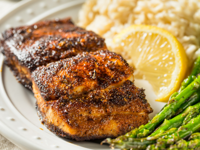 A photo of a white plate topped with blackened fish, rice, asparagus, and a sliced lemon.