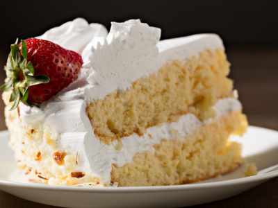 A photo of a slice of cake with white frosting and a strawberry on a white plate.