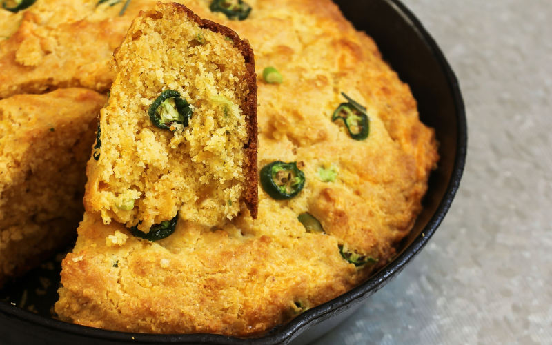 A photo of jalapeño cornbread in a cast iron pan with one slice taken out.