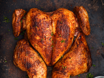 A photo of a full chicken seasoned with poultry seasoning on a dark countertop.