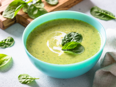 A photo of spinach soup in a blue bowl surrounded by individual pieces of spinach.