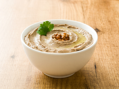 A photo of a bowl of hummus with chickpeas in the center, sitting on wood countertop.