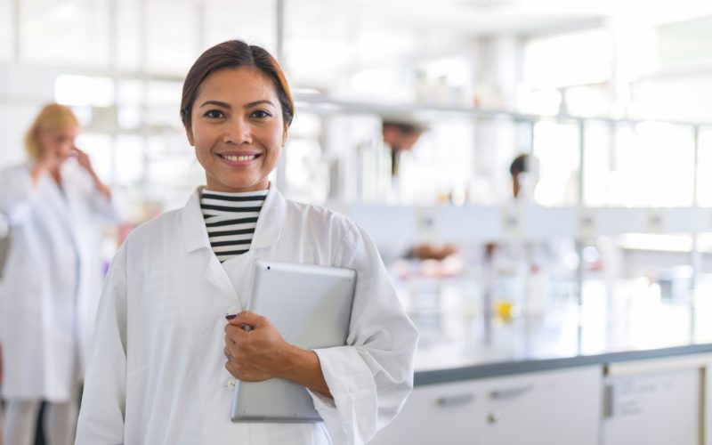 A photo of a woman in a lab coat holding a computer.