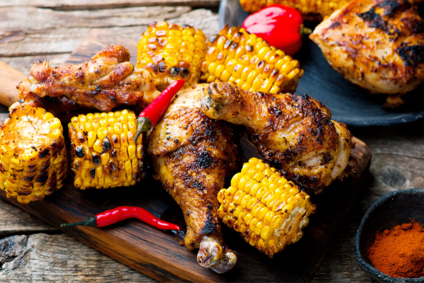 A photo of cajun fried corn on a wooden board with grilled chicken and hot peppers.