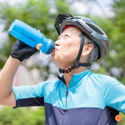 A photo of an older man drinking out of a water bottle with a bike helmet on.