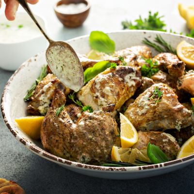 A photo of a bowl of cooked chicken with lemon pepper seasoning. In the bowl, there's also lemons and herbs.