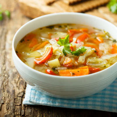 A photo of a white bowl of soup with carrots, peppers, and onions.