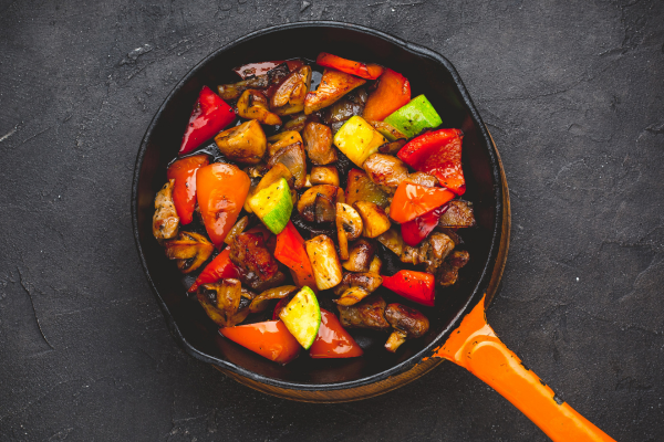 Peppers, mushrooms, and other vegetables mixed in a frying pan on top of a charcoal background, showcasing summer grilling blends.