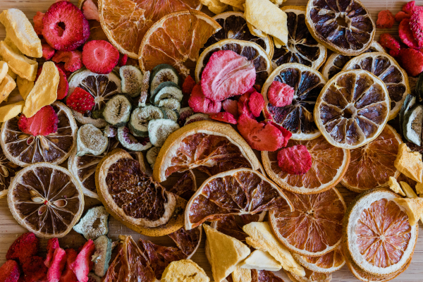 Display of various colorful freeze-dried and dehydrated fruits in bulk bins at a market, including bananas, kiwis, apples, pineapples, mangoes, cherries, and other assorted fruits.
