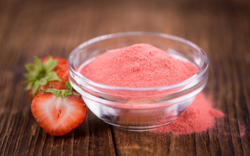 A strawberry fruit powder in a transparent bowl on top of a wooden surface.