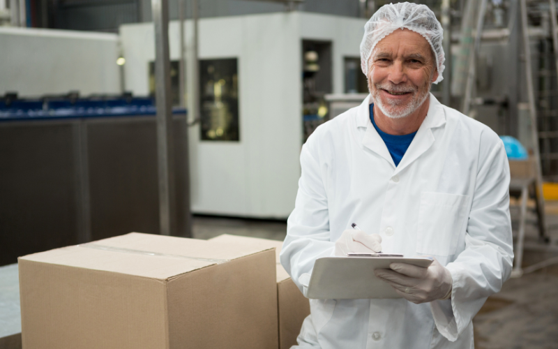 A research and development worker next to a cardboard box in a warehouse lab. The worker is holding a pen.