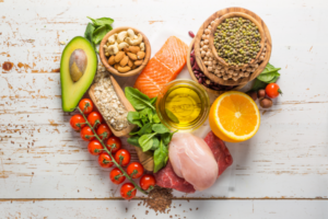 Various gut healthy fruits, vegetables, and meats placed in a heart shape on a white wooded background