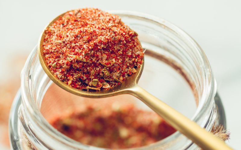 Gold spoon full of a mixed spice blend with a glass jar full of the spice blend in the background