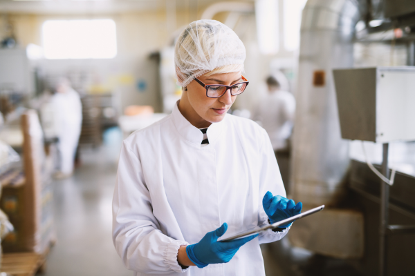 A food production worker next to a cardboard box in a warehouse lab. The worker is holding a pen.