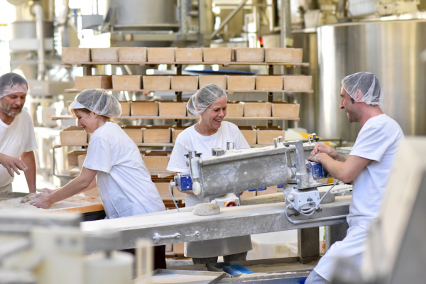 Four workers in hairnets and white clothes using calcium propionate at their commercial bakery for loaves of bread