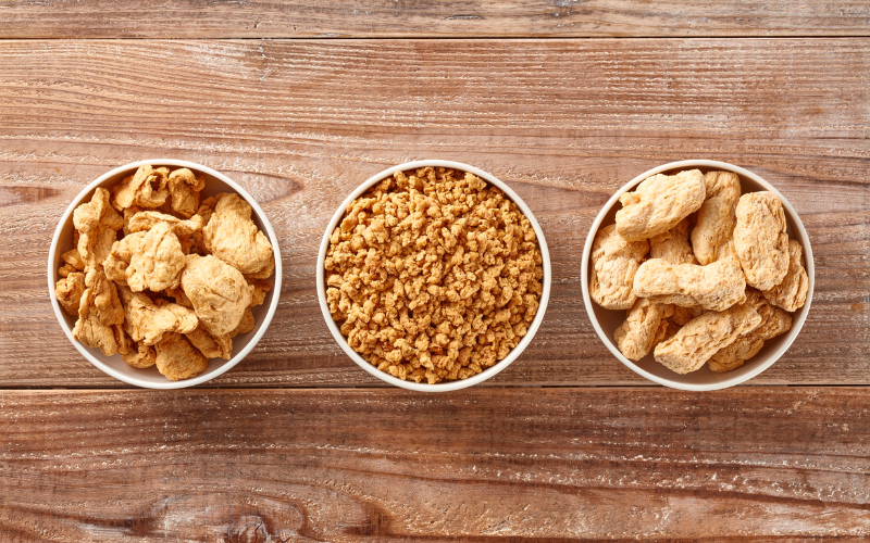3 bowls of soy proteins arranged in a straight horizontal line on a wooden table